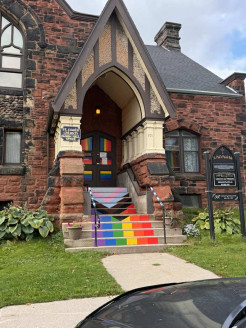 Picture of a church building with a Pride Progress flag painted on their stairs.